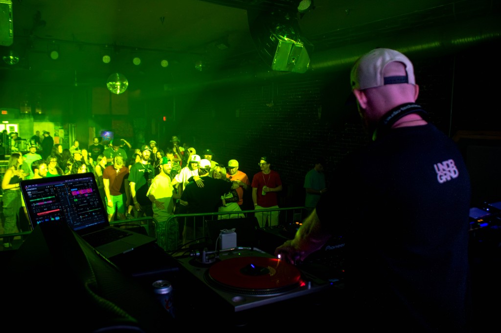 Over the booth — turntable, laptop, crowd behind the barricade