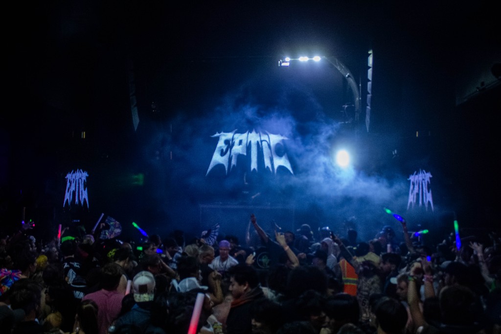 Wide from the hall — EPTIC on triple screens, blue haze
