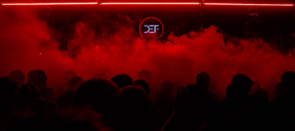 DEF neon through red smoke, crowd in silhouette